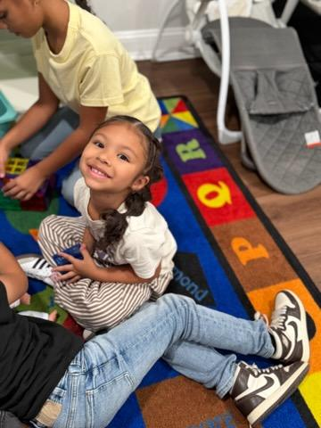 A child sitting on a colorful educational rug playing with magnetic building tiles